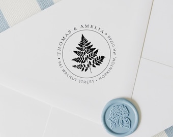 May include: A white envelope with a black circular stamp featuring a fern design. The stamp includes the text "THOMAS & AMELIA" and address details. A light blue wax seal with a floral design is in the lower right corner.