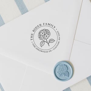 May include: A white envelope with a circular stamp featuring a hydrangea flower and the text "THE RIDER FAMILY" and address details. A light blue wax seal with a hydrangea design is also present.