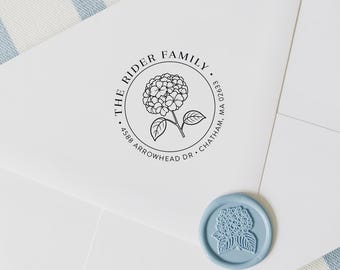 May include: A white envelope with a circular stamp featuring a hydrangea flower and the text "THE RIDER FAMILY" and address details. A light blue wax seal with a hydrangea design is also present.