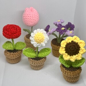 May include: Five crocheted flower plants in small brown pots. The flowers include a red rose, a pink tulip, a white daisy with a yellow centre, purple flowers, and a yellow sunflower with a brown centre.