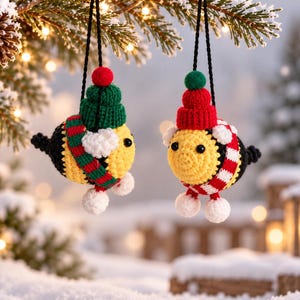 Może przedstawiać: Dwie szydełkowe ozdoby w kształcie pszczół zawieszone na czarnych sznurkach. Każda pszczoła ma żółto-czarny tułów w paski, białe skrzydełka i małe białe stópki. Jedna pszczoła ma zieloną czapkę z czerwonym pomponem i czerwono-zielony szalik, a druga czerwoną czapkę z zielonym pomponem i czerwono-biały szalik.