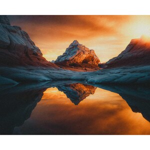 May include: A mountain peak reflected in a still pool of water, with a dramatic orange and red sunset sky in the background.
