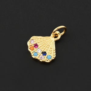 May include: A gold-colored seashell pendant with colorful gemstones. The pendant has a small loop at the top for attaching to a chain or bracelet. The gemstones are orange, pink, red, blue, and turquoise.