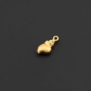 Puede incluir: Un pequeño dije dorado con forma de pincel. El dije tiene un lazo en la parte superior para sujetarlo a un collar o pulsera. Las cerdas del pincel son detalladas y curvadas.