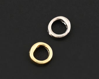 May include: Two small, circular jewelry findings. One is gold-toned, the other is silver-toned. Both are set against a dark background. These findings are likely used in jewelry making or crafting.