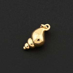 May include: A small, gold-colored seashell charm with a loop at the top for attaching to a necklace or bracelet. The charm has a spiral design and a smooth, polished surface. The background is a solid black.