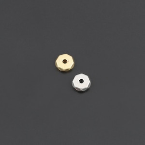 May include: Two small, faceted, circular beads with a central hole. One bead is finished in a metallic gold tone, and the other bead is finished in a metallic silver tone. Both beads feature a geometric, multi-sided edge design.
