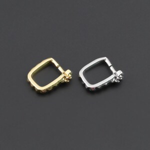 May include: Two small hoop earrings, one in a gold tone and one in a silver tone. Each earring features a square-like shape with rounded corners and a small decorative cluster of tiny stones or beads at the hinge closure mechanism.