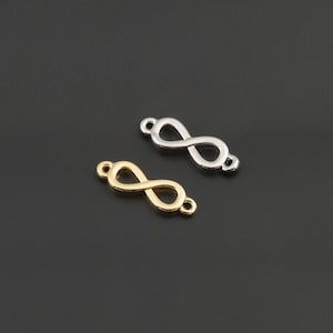 May include: Two small infinity symbol charms, one in a polished gold tone and one in a polished silver tone. Each charm features a continuous loop design with a small circular connector loop at both ends, suitable for jewelry making components.