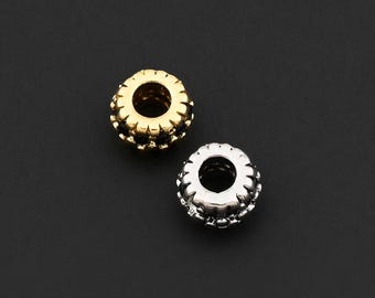 Peut inclure: Deux petites perles rondes avec un motif décoratif et texturé. Une perle est de couleur or et l'autre est de couleur argent. Les perles ont un trou au centre et sont posées sur un fond sombre.