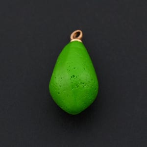 May include: A bright green, teardrop-shaped pendant with a textured surface. The pendant has a small, gold-colored loop at the top for hanging. The background is a solid, dark gray.