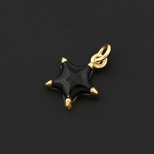 May include: A small, gold-colored star pendant with a black enamel center and gold-colored tips. The pendant has a loop for attaching to a chain or bracelet. The star is set against a dark background.