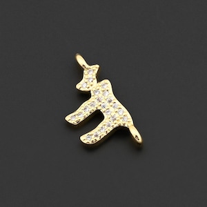 May include: A gold-colored pendant in the shape of a stylized animal, possibly a deer or elk. The pendant is encrusted with small, clear gemstones, giving it a sparkling appearance. The background is a solid, dark gray.