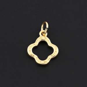 May include: A gold-colored clover charm pendant with a four-leaf design. The charm has a small loop at the top for attaching to a chain or bracelet. The pendant is set against a black background.