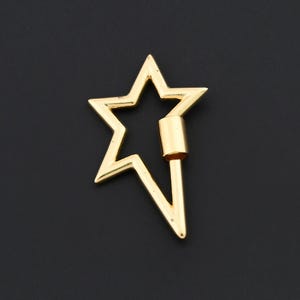 May include: A gold-coloured star-shaped clasp against a black background. The clasp has a simple, open star design with a secure locking mechanism. The star's points are sharp and defined, and the metal has a polished finish.