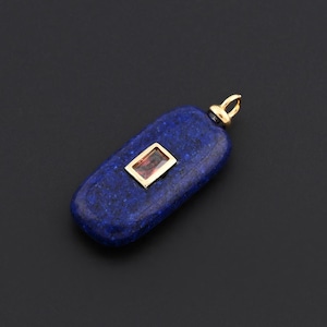 May include: A dark blue pendant with a rectangular, reddish-brown stone set in a gold frame. The pendant has a gold bail and is set against a black background. The gemstone is centered on the pendant.