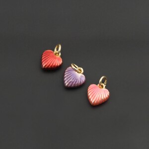 May include: Three small heart-shaped charms featuring a ribbed, textured surface. Each charm is finished in a different metallic color: one deep red, one purple, and one light pink. Each heart includes a small gold-toned jump ring at the top.
