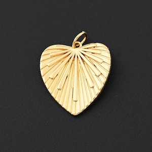 May include: A gold-colored heart-shaped pendant with a textured, fan-like design. The pendant has a small loop at the top for attaching to a chain. The heart is set against a dark background.