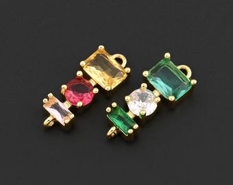 May include: Two gold-toned jewelry charms with colorful rectangular and round gemstones. One charm features pink, red, and yellow stones. The other has green, white, and green stones. The charms are set against a black background.