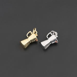 May include: Two small metal charms shaped like moka pot coffee makers, one finished in a polished gold tone and the other in a polished silver tone. Each charm features a handle, a spout, and a small circular jump ring at the top for attachment.