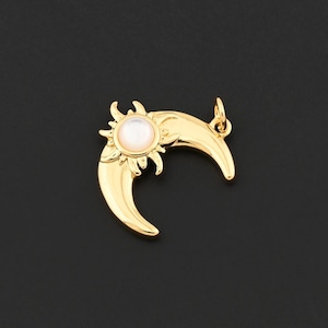 May include: A gold-colored pendant featuring a crescent moon design with a sunburst and a central, round, off-white stone. The pendant has a small loop for a chain and is set against a black background.