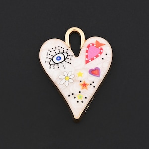 May include: A heart-shaped charm with a gold-colored border. The charm is white with colorful illustrations, including an eye, a daisy, stars, and hearts. The charm has a small loop at the top for attaching to a necklace or bracelet.