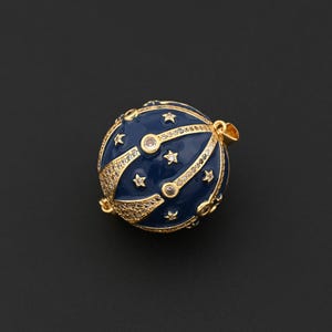 May include: A spherical pendant with a dark blue enamel finish, adorned with gold-colored accents and small star-shaped details. The pendant features a gold-colored bail for hanging and is embellished with clear crystals.