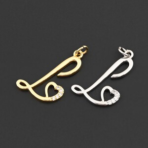 May include: Two metal letter "L" charms, one gold-toned and one silver-toned, each with a heart-shaped embellishment. The hearts are encrusted with small, clear crystals. The charms are designed for jewelry making.