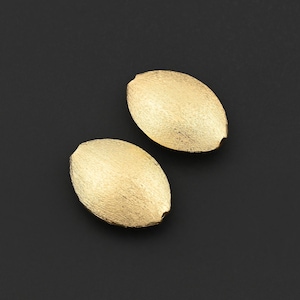 Può includere: Due orecchini ovali color oro con superficie strutturata sono esposti su uno sfondo scuro. Gli orecchini hanno una piccola rientranza su un lato. I gioielli sono probabilmente in metallo.