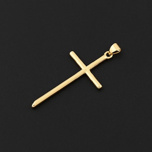 May include: A gold-colored pendant in the shape of a cross. The cross has a simple, elongated design with a loop at the top for a chain. The background is a solid black.