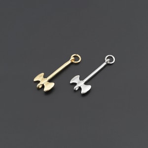 May include: Two metal axe charms, one in a gold tone and one in a silver tone. Each charm features a double-bladed axe head attached to a long handle with a small circular jump ring at the top for attachment to jewelry or other craft projects.