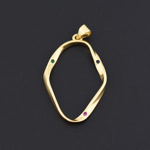 May include: A gold-colored pendant with an abstract, twisted oval design. The pendant features three small gemstones: green, blue, and pink, set along the edges. The bail is integrated into the design. The background is a solid black.