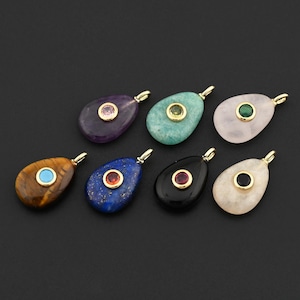 May include: Seven teardrop-shaped gemstone pendants in various colors, including purple, blue, green, and black. Each pendant features a gold-colored bail and a smaller, contrasting gemstone set in the center. The gemstones include amethyst, lapis lazuli, and tiger's eye.