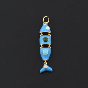 May include: A blue and gold fish-shaped pendant with a gold loop at the top. The pendant has a light blue enamel finish with gold accents and features three gemstone accents: a white, a green, and a turquoise stone. The fish tail has a peach-colored stone.