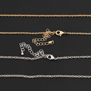 May include: Close-up of gold and silver-colored necklaces with lobster claw clasps and extender chains. The necklaces are displayed against a black background. The chains have a delicate, twisted rope design.