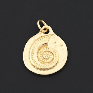 May include: A gold-coloured pendant featuring a spiral design, reminiscent of a nautilus shell, set against a black backdrop. The pendant has a textured surface and a small loop at the top for attaching to a chain or cord.