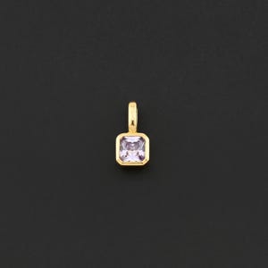 May include: A gold pendant with a square, light purple gemstone. The gemstone is set in a gold bezel. The pendant has a small loop at the top for a chain. The background is solid black.