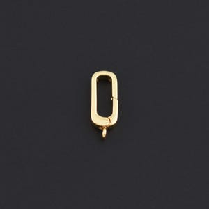 May include: A gold-colored, rectangular clasp with a small loop at the bottom. The clasp is open, revealing the interior. The background is a solid black.