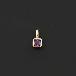 May include: A gold pendant with a square, purple gemstone. The gemstone is set in a gold bezel and has a rectangular shape. The pendant has a small loop at the top for a chain.