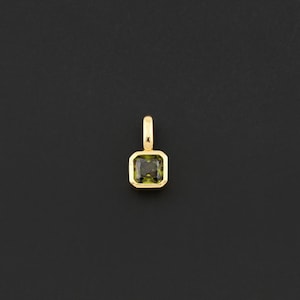 May include: A gold pendant with a square, olive-green gemstone. The pendant has a simple, elegant design with a small loop at the top for a chain. The gemstone is set in a gold bezel, creating a classic and timeless look.