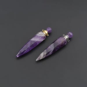 May include: Two pointed, faceted amethyst crystal pendants with a conical shape. Each pendant features a small, round amethyst bead stopper at the top, secured by a metal cap with a small loop for attachment, one in gold tone and one in silver tone.