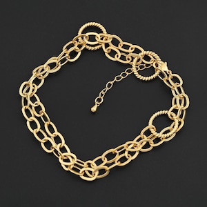 May include: Gold-toned necklace with a double-strand chain design. The necklace features oval-shaped links with textured detailing, connected by smaller, twisted ring accents. An adjustable chain and lobster clasp complete the piece.