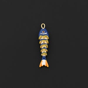 May include: A blue fish-shaped pendant with gold accents and an orange and white tail. The pendant has a small red gem for an eye and a gold loop at the top for hanging. The fish design is detailed and colorful.