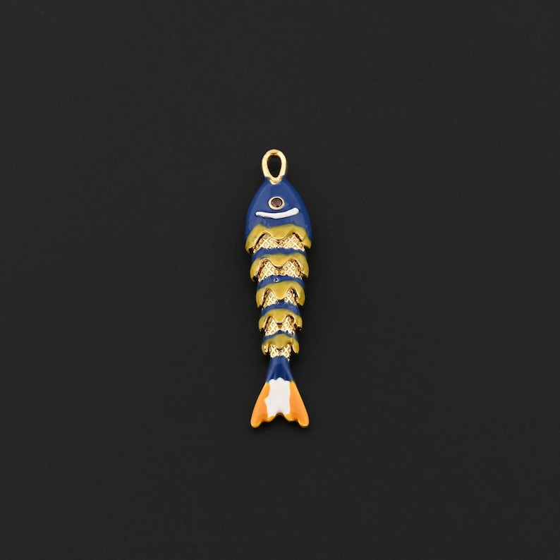 May include: A blue fish-shaped pendant with gold accents and an orange and white tail. The pendant has a small red gem for an eye and a gold loop at the top for hanging. The fish design is detailed and colorful.