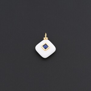 May include: A white, diamond-shaped pendant with a gold bail. The pendant features a square, deep blue gemstone set in the centre. The pendant is set against a dark background.
