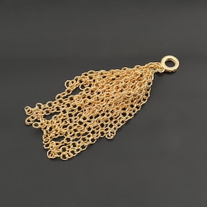 May include: A gold-toned metal tassel pendant composed of numerous delicate, interconnected circular chain links. The chains are gathered together and attached to a single, solid circular ring at the top, creating a cascading, layered effect.