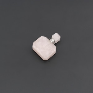 Puede incluir: Un frasco de perfume de cuarzo rosa pálido con un cuerpo rectangular facetado y un pequeño tapón cuadrado. El frasco presenta un cuello de metal plateado que conecta el cuerpo principal de piedra con el tapón de piedra rosa a juego.