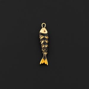 May include: A gold-colored fish pendant with black accents. The pendant has a loop at the top for hanging and a detailed, layered design. The tail and head are gold, and the body is black with gold trim.