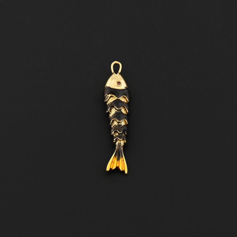 May include: A gold-colored fish pendant with black accents. The pendant has a loop at the top for hanging and a detailed, layered design. The tail and head are gold, and the body is black with gold trim.