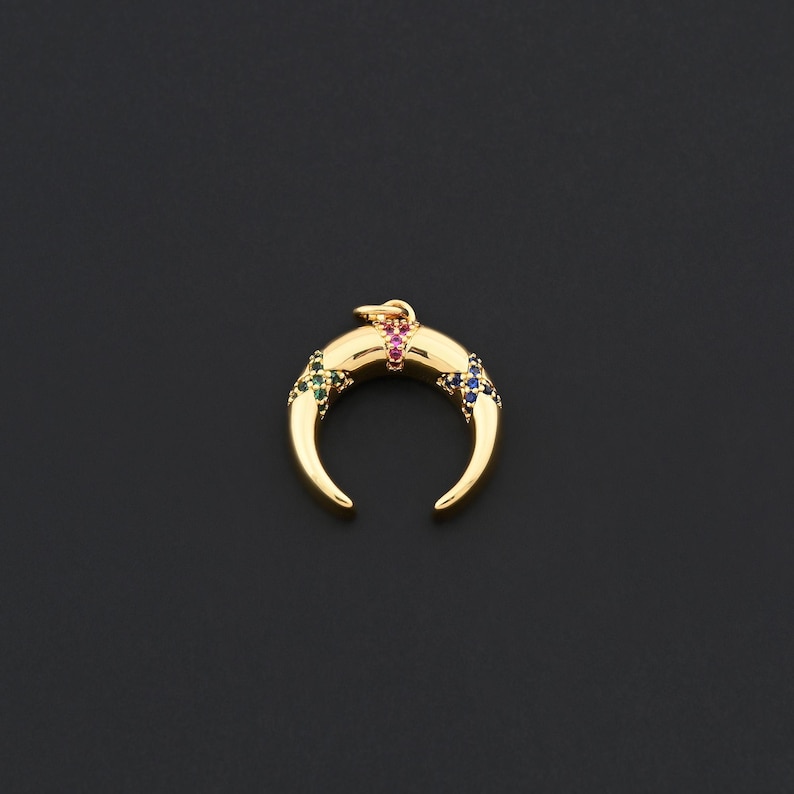 K&ouml;nnte beinhalten: Goldfarbener Halbmond-Anh&auml;nger mit bunten Edelsteinen. Der Anh&auml;nger hat eine gebogene Form mit einer Schlaufe f&uuml;r eine Kette. Die Edelsteine sind in Rot, Gr&uuml;n und Blau gehalten und verleihen dem Gold Farbe. Der Anh&auml;nger ist vor dunklem Hintergrund platziert.
